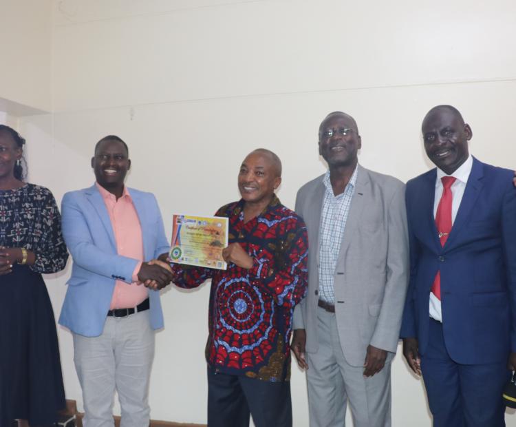 Alton Kogo (2nd Left), Director North Rift, Micro and Small Enterprises Authority (MSEA), hands over a certificate of participation to Richard Muteti, Chairman of the Skilled Artisans and Informal Apprenticeship Association-Kenya Chapter. They are flanked by Antoninah Makoba (Left), Chairlady of Fashions and Design Association, John Onyango (3rd Right), KIPI MD and  Richard Opar (2nd Right), KNFJKA Secretary General, Uasin Gishu Chapter during the closing ceremony of the Workshop